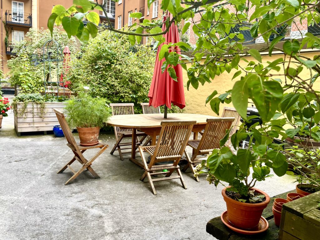 Innergård med gemensam uteplats, bord, stolar och växter i krukor.